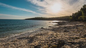 A rocky beach with clear water and a distant tree-covered hill under a bright sky. - Holiday apartment only 150 m to the Adriatic Sea (Mali Lošinj)