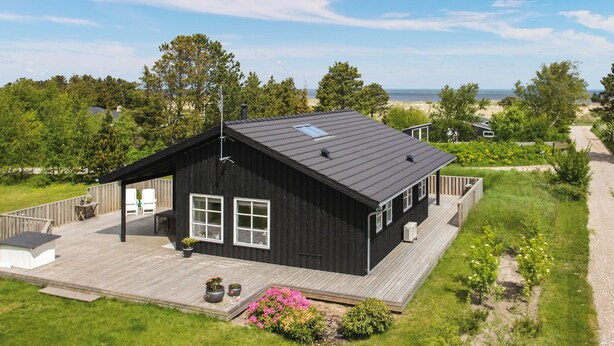 A black wooden cabin with a deck, large windows, and a view of the beach and ocean. - Cozy home in Frederikshavn with kitchen (Frederikshavn)