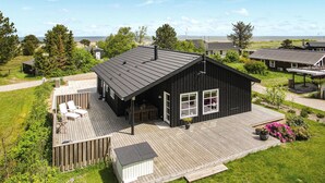 A black wooden house with a sloped roof, a deck, and a small garden area. - Cozy home in Frederikshavn with kitchen (Frederikshavn)
