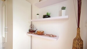 Une pièce au style minimaliste, avec des murs blancs, une porte blanche et une étagère blanche agrémentée d’objets décoratifs.