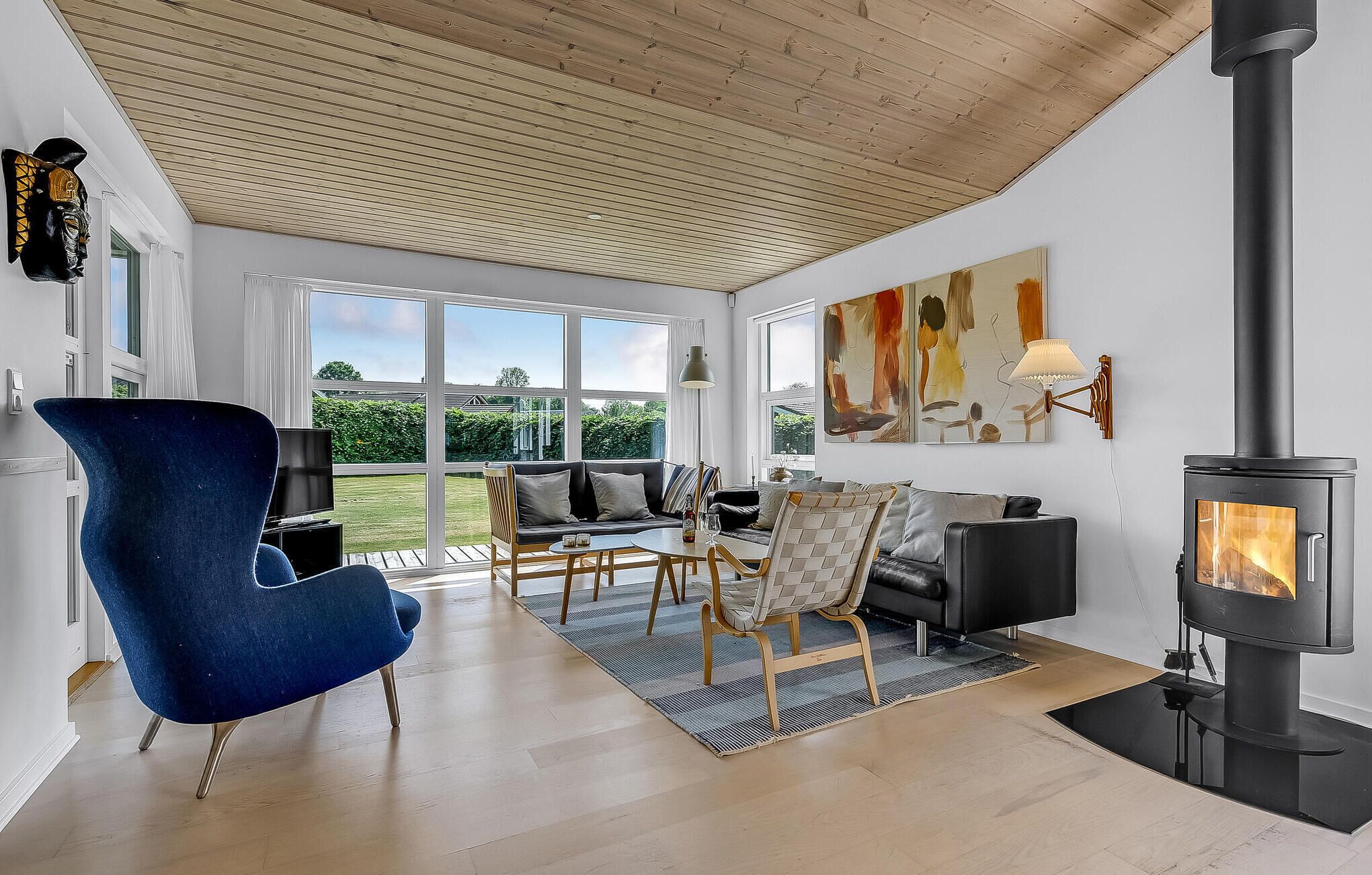A spacious living room with a large window, a black wood-burning stove, and a blue armchair.