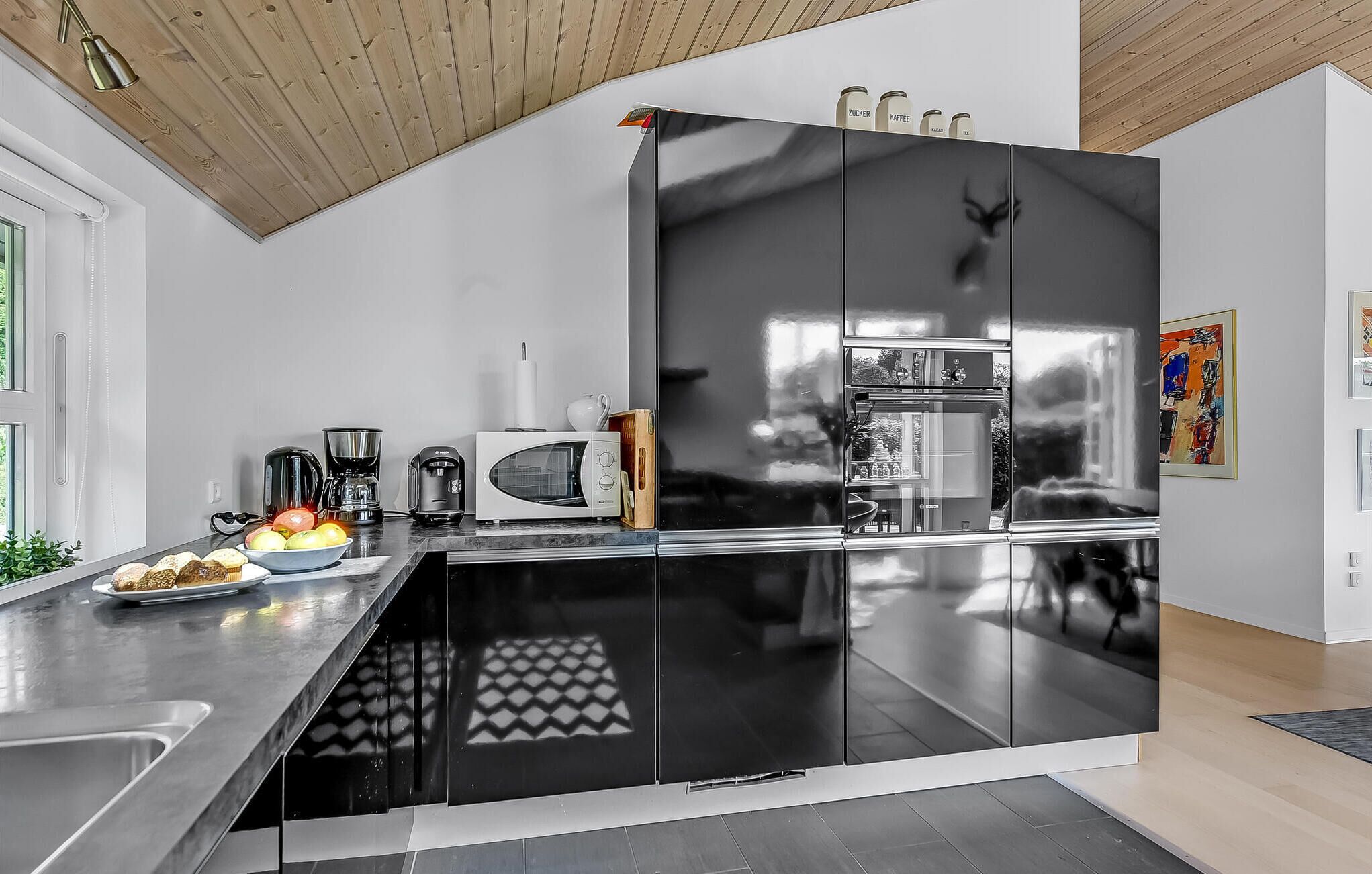 Une cuisine moderne aux couleurs noir et blanc, dotée d’appareils électroménagers en acier inoxydable et d’un plafond en bois.