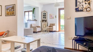 Un salon comprenant un canapé, un téléviseur, une table à manger et un coin cuisine avec un meuble et une fenêtre.