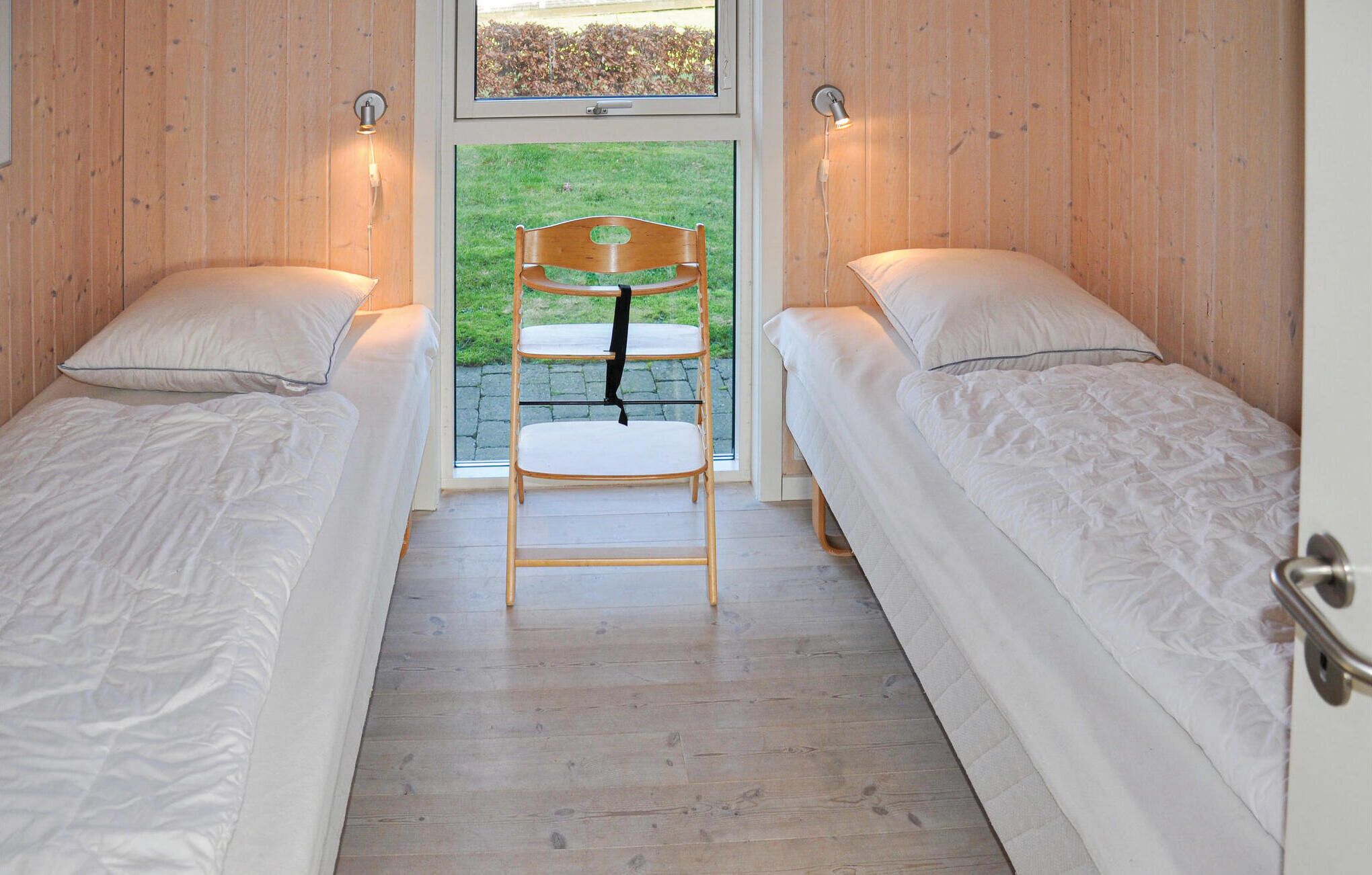 Una habitación con dos camas individuales, una silla de madera y una ventana con vistas a un jardín.