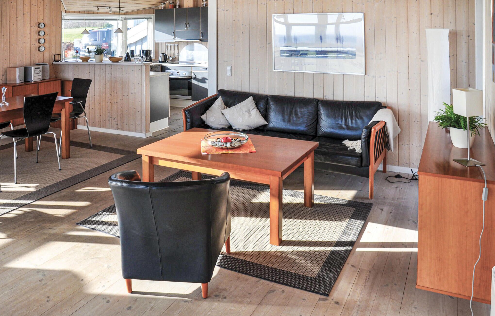 A modern living room with a black leather sofa, wooden coffee table, and a dining area with a wooden table and chairs.
