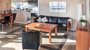 A modern living room with a black leather sofa, wooden coffee table, and a dining area with a wooden table and chairs.