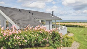 A modern house with a grey roof, a covered porch, and a view of the sea.