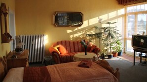 Une chambre d’hôtel avec un lit, un canapé, une petite table, un radiateur, une télévision et plusieurs plantes en pot.