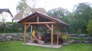 Un kiosque en bois doté d’un four en briques, entouré d’un mur de pierres et de verdure.