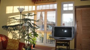 Un salon avec un téléviseur, une plante en pot et une fenêtre équipée de stores.