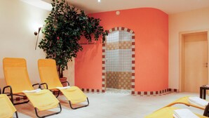 Una habitació d'spa amb cadires grogues, una planta gran en test, una paret amb rajoles i una porta.