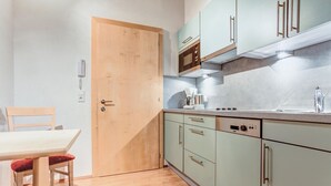 Una cuina compacta amb armaris de color verd clar, una porta de fusta i una zona de menjador amb taula i cadires.