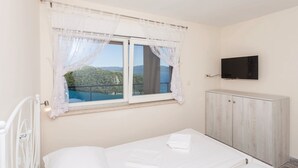 A bedroom with a bed, a TV mounted on the wall, and a window with a view of greenery and mountains.