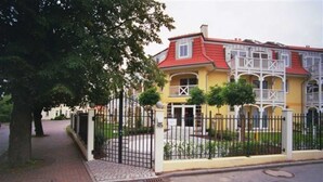 A yellow building with a red roof, white balconies, and a gated entrance. - (191) 2-room apartment - apartment house Baltic Sea beach (Kühlungsborn)
