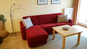 A red sofa with a small table and a floor lamp in a room with two framed pictures on the wall. - (191) 2-room apartment - apartment house Baltic Sea beach (Kühlungsborn)