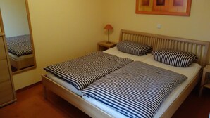 A bedroom with a bed, a nightstand, a lamp, a mirror, and a framed picture on the wall. - (191) 2-room apartment - apartment house Baltic Sea beach (Kühlungsborn)