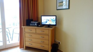 A room with a television on a wooden cabinet, a framed picture on the wall, and a sliding glass door leading to an outdoor area. - (191) 2-room apartment - apartment house Baltic Sea beach (Kühlungsborn)