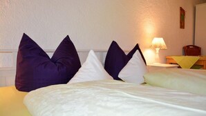 Un lit avec des oreillers blancs et violets, une lampe et une chaise en bois.