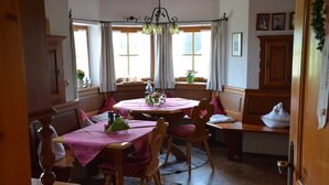 Un espace repas comprenant une table ronde, des chaises en bois, un lustre et une vue sur l’extérieur grâce à de grandes fenêtres.