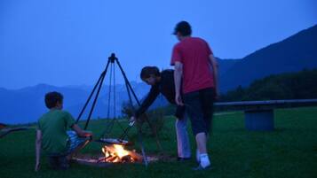 An outdoor setting with a fire pit, grassy area, and mountains in the background.