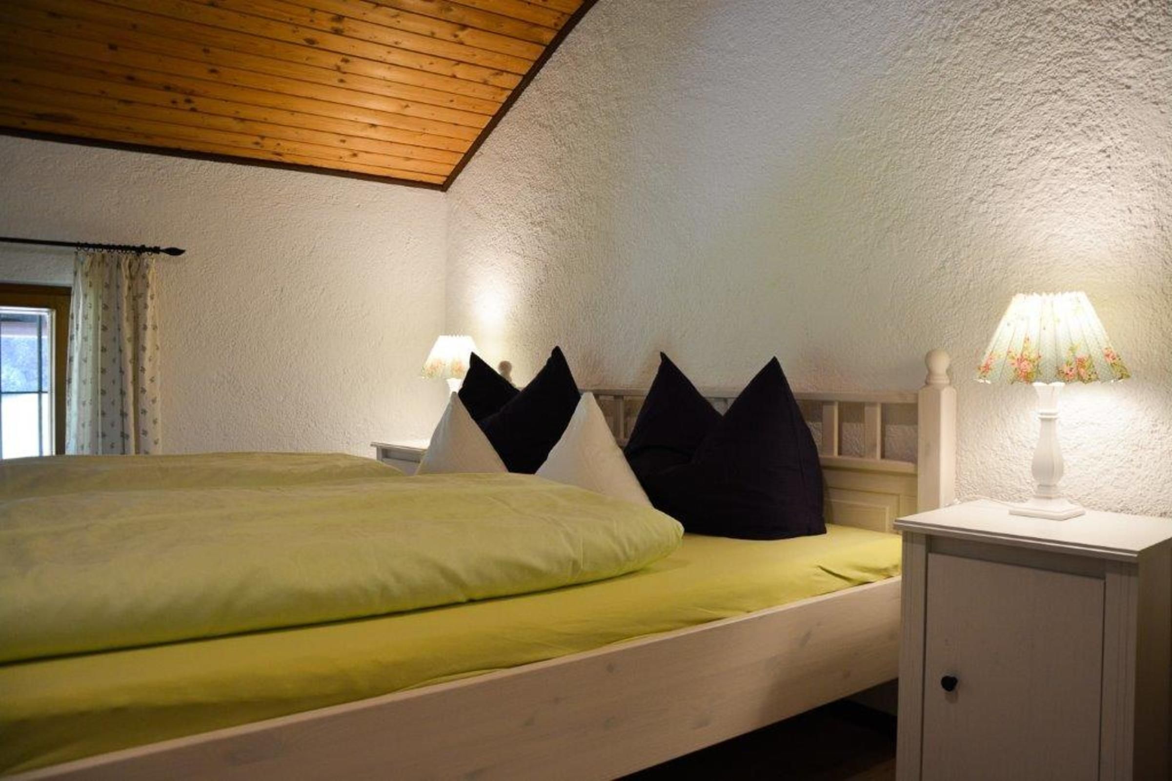 Ein Einzelbett mit grüner Tagesdecke, ein weißer Nachttisch mit Lampe und ein weißer Kleiderschrank.