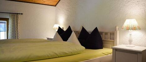 A single bed with a green bedspread, a white nightstand with a lamp, and a white wardrobe.