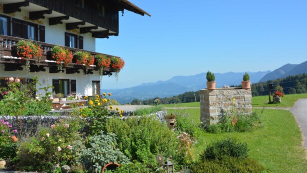 Un chalet traditionnel doté d’un balcon orné de fleurs, d’un mur en pierre et offrant une vue sur les montagnes.