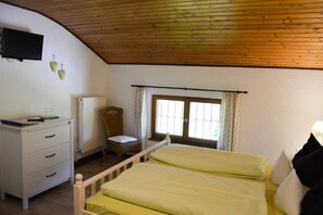 A bedroom with a wooden ceiling, a bed with yellow bedding, a white dresser, a chair, a radiator, and a window with curtains. - Double room Hollerbeerl - Hof Roßruck (Fischbachau)