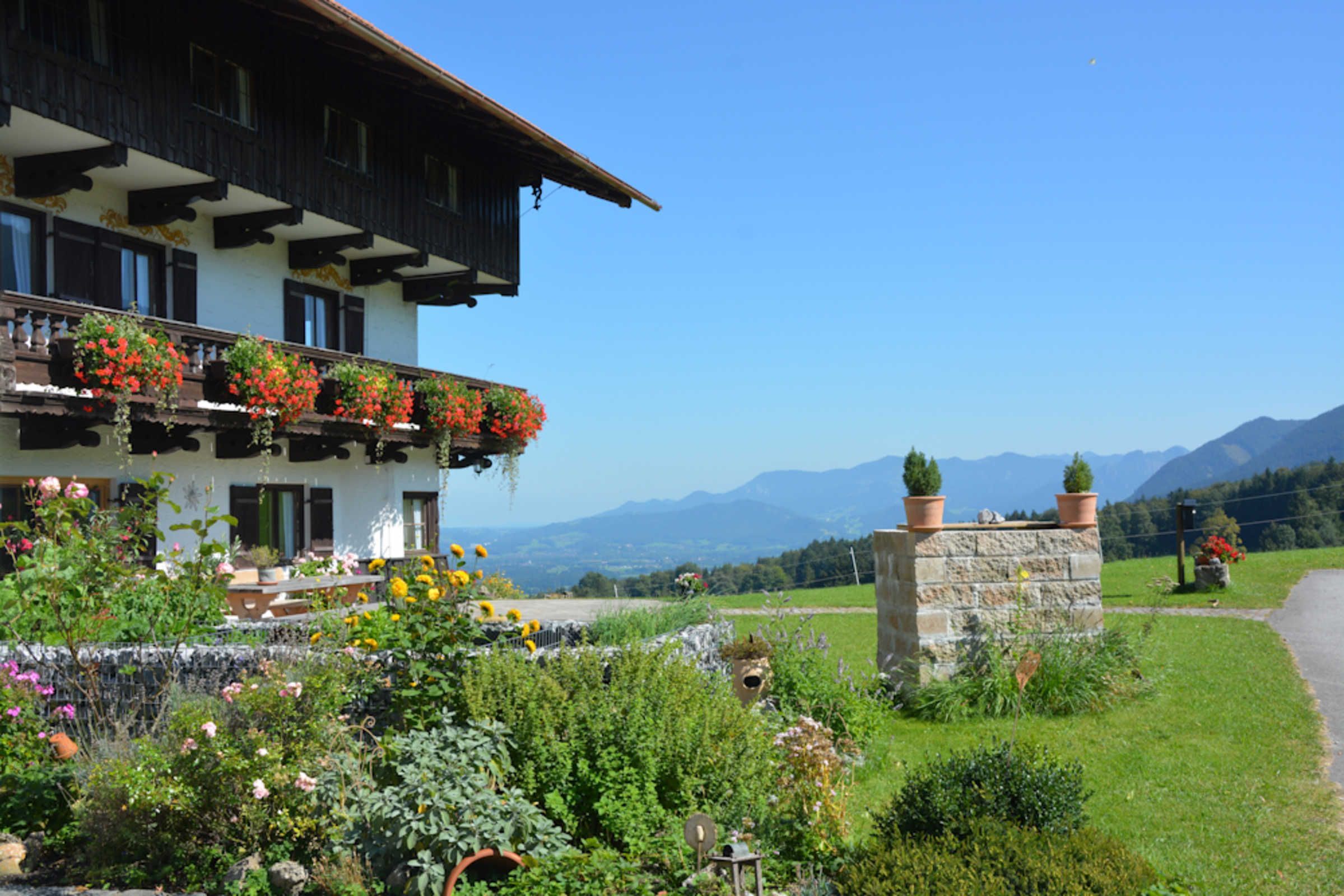 Ein traditionelles Chalet mit einem Balkon, der mit Blumen geschmückt ist, einer Steinmauer und Bergblick.