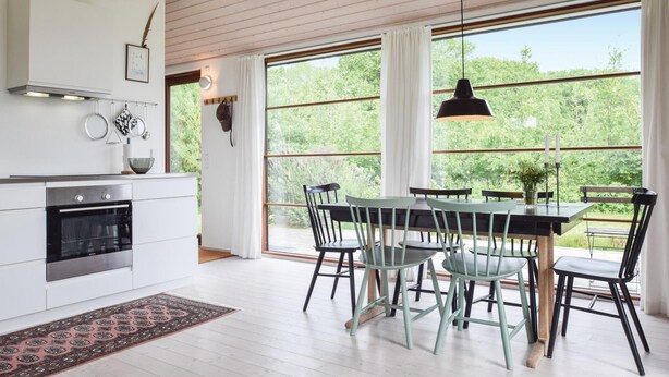Une cuisine moderne avec des meubles blancs, un four noir et un coin repas comprenant une table et des chaises en bois.
