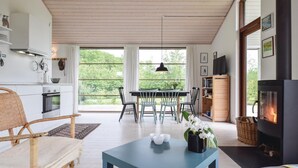 Un salon moderne comprenant un coin repas, une cheminée et de grandes fenêtres donnant sur un espace verdoyant.