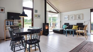 Un vaste espace de vie doté d’un haut plafond, d’une cheminée, d’une table à manger avec des chaises, d’un canapé et d’un téléviseur.