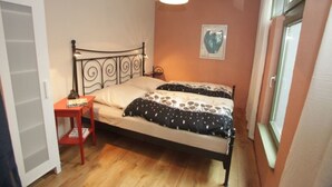 Un dormitorio con cama, mesita de noche, ventana y puerta.