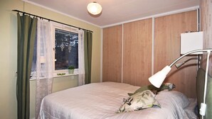 Une chambre à coucher avec un lit, une fenêtre avec des rideaux, une lampe de chevet et une petite plante posée sur le rebord de la fenêtre.