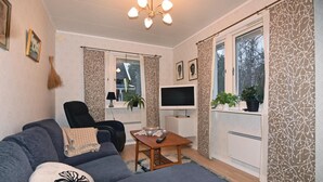 Un salon comprenant un canapé, un fauteuil, un téléviseur et une petite table sur laquelle sont posées les télécommandes.