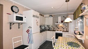 Une cuisine de taille réduite avec des meubles blancs, un four à micro-ondes, une cuisinière et une table à manger recouverte d’une nappe à motifs.