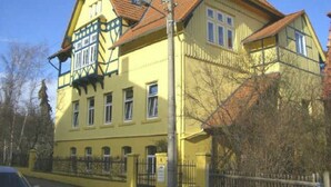 Un bâtiment à deux étages, doté d’une façade jaune, de nombreuses fenêtres et d’un toit recouvert de tuiles rouges.