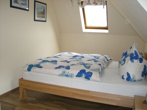 A single bed with a floral bedspread and matching pillow in a room with wooden flooring, a small skylight, and two framed pictures on the wall.