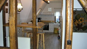 Une cuisine rustique avec des poutres en bois, une table à manger avec des chaises, un luminaire suspendu et une vue sur le salon.