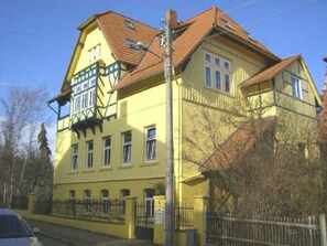 Ein zweistöckiges Gebäude mit gelber Fassade, zahlreichen Fenstern und einem roten Ziegeldach.