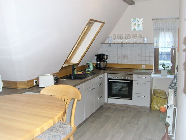 A kitchen with a dining table, chairs, a coffee maker, and an oven. - Vacation apartment Villa am Wald (Blankenburg (Harz))
