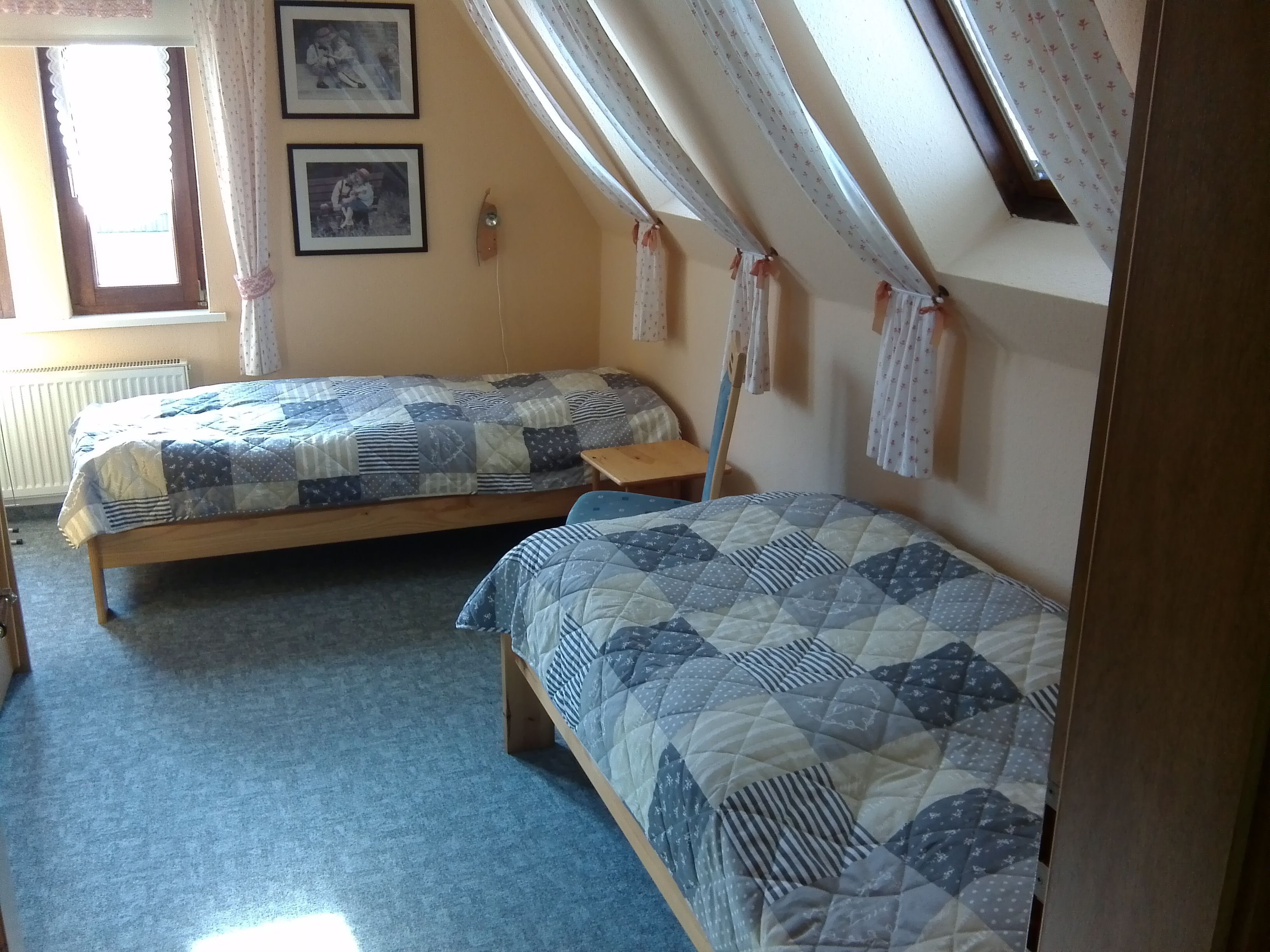A dormitory room with two single beds, a wooden floor, a radiator, and a window with curtains.