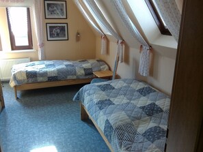 A dormitory room with two single beds, a wooden floor, a radiator, and a window with curtains.