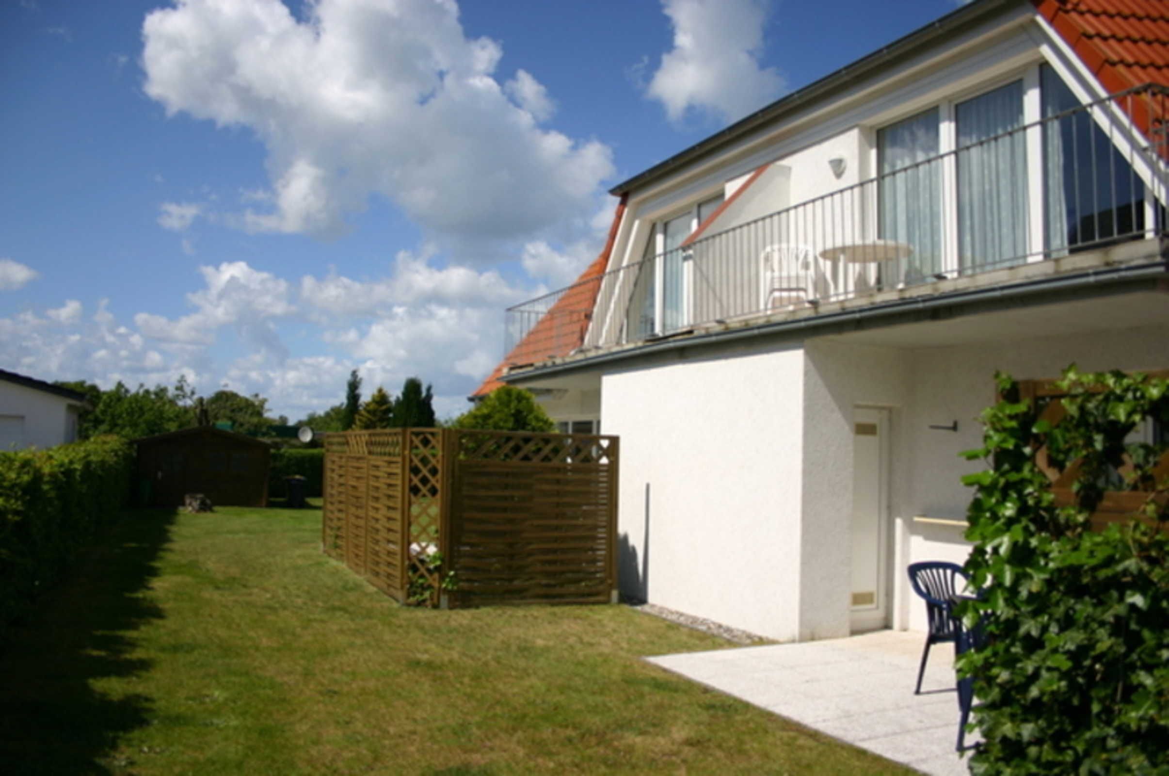 Ein zweistöckiges Haus mit Balkon, kleinem Garten und Holzlattenzaun.