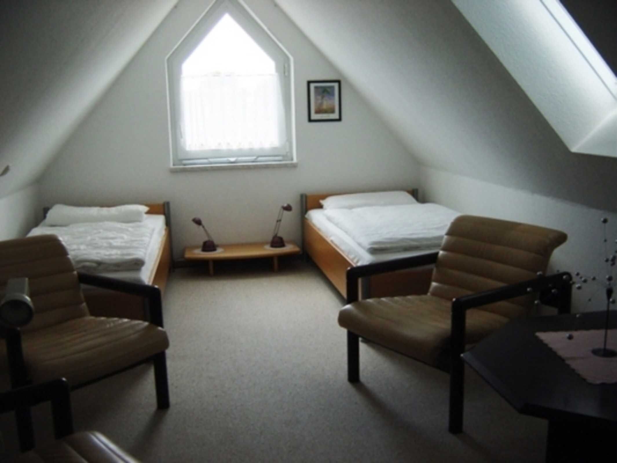 Ein kleines, dreieckiges Schlafzimmer im Dachgeschoss mit zwei Betten, einem Fenster und einem Schreibtisch.