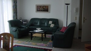 Ein Wohnzimmer mit einem grünen Sofa, einem Couchtisch, einem gemusterten Teppich und einem Bild an der Wand.