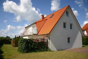 Ein zweigeschossiges Haus mit rotem Ziegeldach, einer Satellitenschüssel und einem umzäunten Garten.