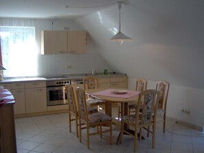 A kitchen with a dining table, chairs, a stove, and a hanging light fixture. - Apartment 1 floor - house gallery (Karlshagen)