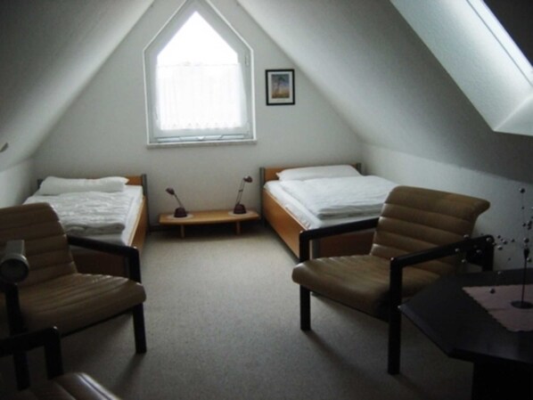 A small, triangular attic bedroom with two beds, a window, and a desk. - Apartment 1 floor - house gallery (Karlshagen)