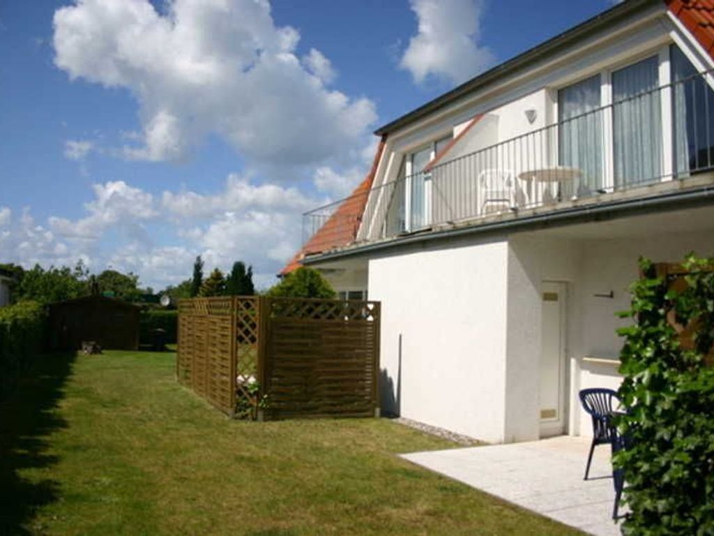 Ein zweistöckiges Haus mit Balkon und einem umzäunten Garten, strahlend blauer Himmel.